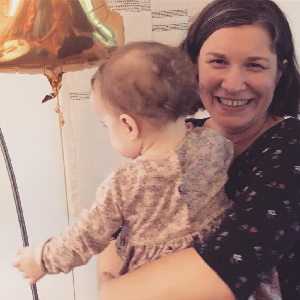 Christa smiling at the camera and holding her one year old