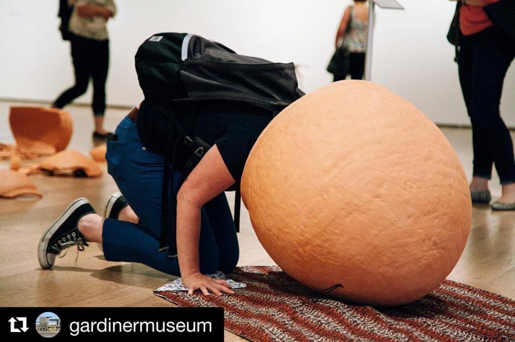 A person is on the ground leaning into a large ceramic pot. The image is tagged "gardinermuseum"
